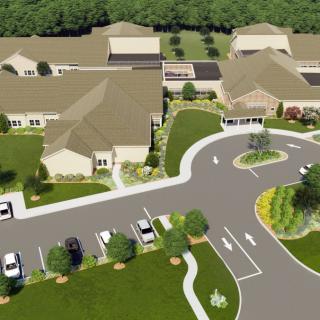 Aerial view of a complex with multiple buildings, surrounded by landscaped greenery and a parking lot.