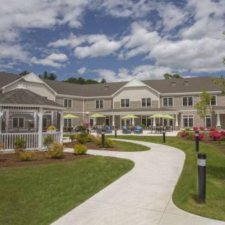 A picturesque residential building with a neat pathway and well-maintained landscaping under a partly cloudy sky.