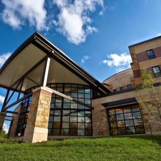 A modern architectural design featuring a combination of glass and stone elements, set against a blue sky.