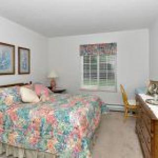 A cozy bedroom with floral bedding, a wooden dresser, and a window letting in natural light.