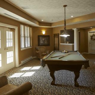 A cozy billiard room with a pool table, seating, and warm lighting.