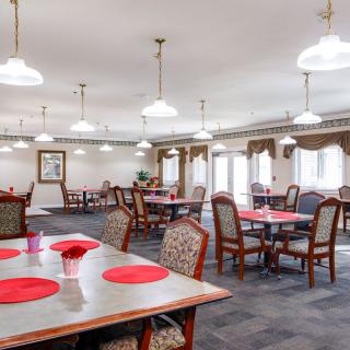 A spacious dining room with neatly arranged tables and chairs, illuminated by ceiling lights.