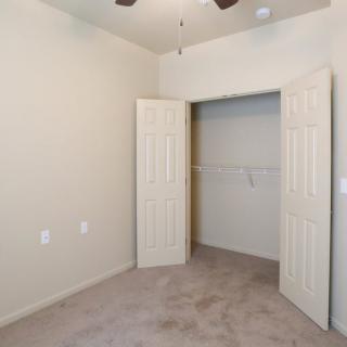 An empty room with an open closet and carpeted flooring, featuring a ceiling fan.