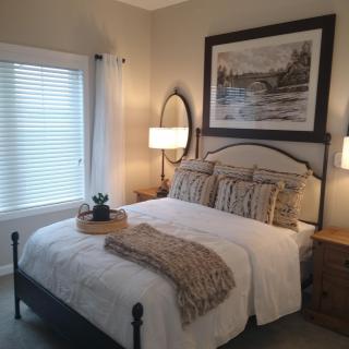 A cozy bedroom with elegant decor, featuring a neatly made bed, flanked by lamps and adorned with framed artwork.