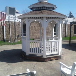 A charming white gazebo in a sunny outdoor setting, complemented by an American flag in the background.