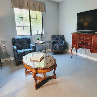 A cozy living room featuring a pair of patterned chairs, a wooden coffee table with glass top, and a television on a vintage cabinet.