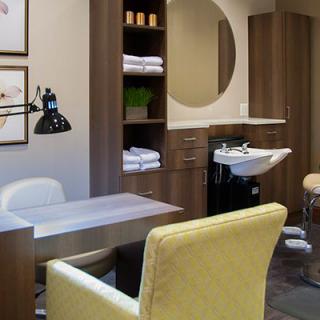 A cozy and well-organized salon interior featuring a chair, desk, mirror, and sink.