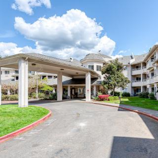 A residential building with a covered entrance and well-maintained landscaping under a partly cloudy sky.