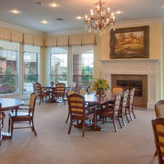 A spacious dining room with multiple tables and chairs, adorned with a chandelier and a fireplace, surrounded by large windows.