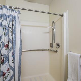 A bathroom featuring a shower with a blue patterned curtain, grab bars, and a towel rack.