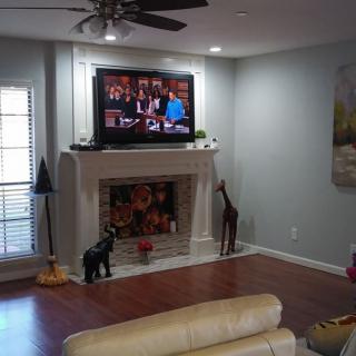 A modern living room featuring a fireplace with a TV mounted above it, giraffe statues on either side, and wooden flooring.