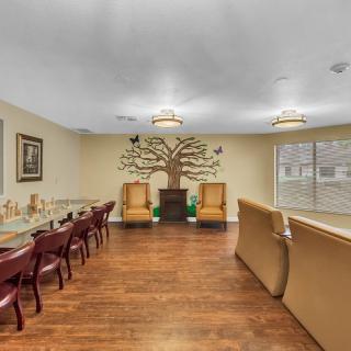 A well-lit living room with wooden flooring, featuring a tree mural on the wall, cozy chairs, and a sofa.