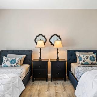 A cozy bedroom with twin beds, each flanked by a nightstand and lamp, featuring stylish decor and patterned pillows.