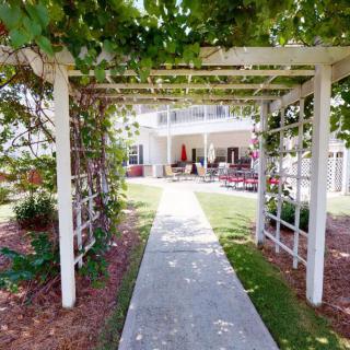 A charming garden pathway leads to an outdoor seating area under a pergola adorned with lush vines.
