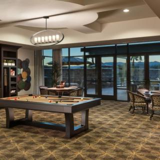 A modern game room featuring a shuffleboard table, stylish furnishings, and large windows allowing natural light.