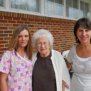 Three women posing together outside in front of a brick building.