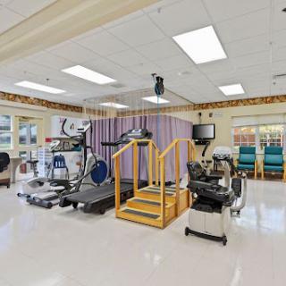 A well-equipped rehabilitation therapy room featuring exercise machines and a set of stairs for patient mobility training.