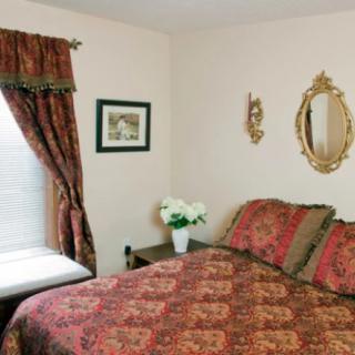 A traditional bedroom with ornate bedding and curtains, featuring a mirror and framed picture on the wall.