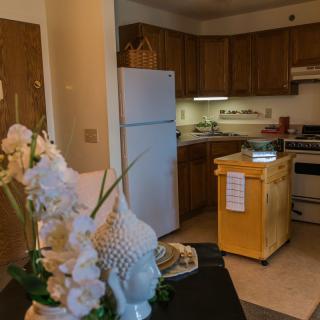 An apartment kitchen with wooden cabinetry, a refrigerator, stove, and decorative elements on the counter.