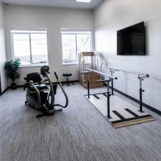A clean and well-lit therapy room with exercise equipment and a large television on the wall.