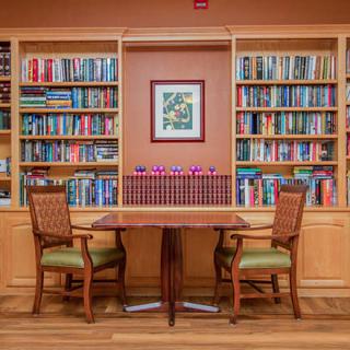 A cozy library corner with wooden bookshelves filled with books, along with a table and two chairs.