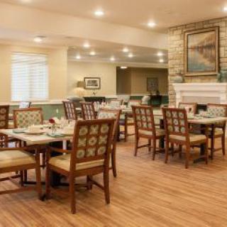 A cozy dining area with neatly arranged tables and chairs, featuring warm lighting and wooden floors.