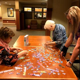 Three individuals engage in assembling a colorful puzzle together.
