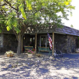 A charming stone house with a welcoming front porch and an American flag, surrounded by greenery.
