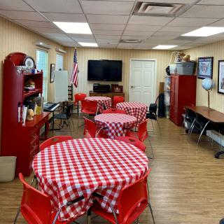 A cozy dining area with red checkered tablecloths and matching chairs, featuring a TV on the wall.