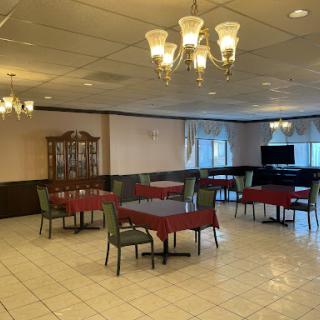 A spacious dining area with tables set for guests, elegantly adorned with chandeliers and a decorative cabinet.