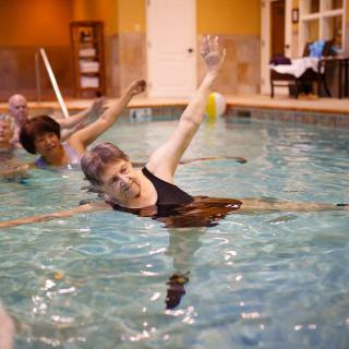 A group of seniors participating in a water aerobics class at an indoor pool.
