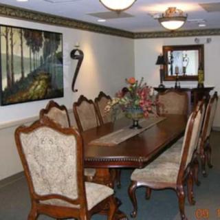 A formal dining room with a long wooden table and upholstered chairs, featuring a wall painting and mirror.