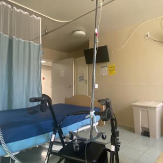 A view of a hospital patient room featuring a bed, walker, and medical equipment.