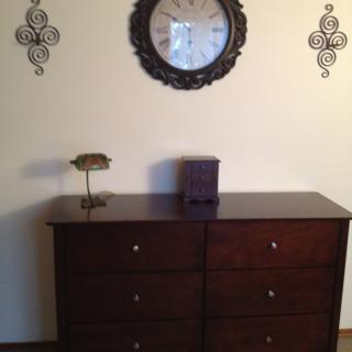 A wooden dresser beneath a decorative wall clock and ornate wall decals.