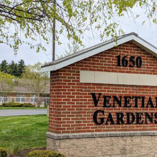 Entrance sign of Venetian Gardens, featuring a well-maintained landscape.