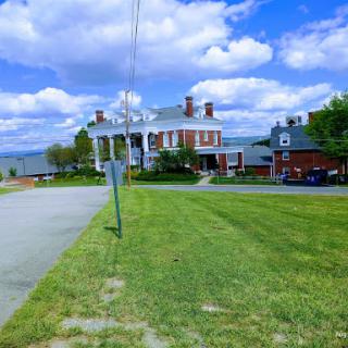 A grand architectural structure against a backdrop of blue skies and fluffy clouds, surrounded by well-maintained grass and a road.