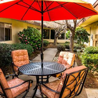 A cozy outdoor patio setting with a table, four cushioned chairs, and a large red umbrella.