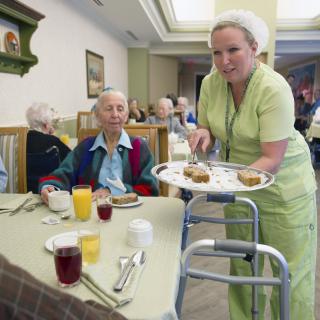 A healthcare worker serving meals to seniors in a nursing home.