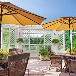 A sunny patio with wicker furniture and large umbrellas, surrounded by a garden setting.