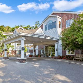 A residential building entrance with a driveway, surrounded by trees and under a clear blue sky.