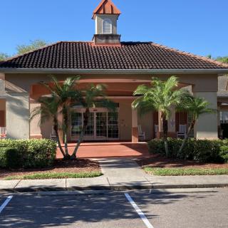 A commercial building with a tiled roof and palm trees in front, viewed from a parking lot during the day.