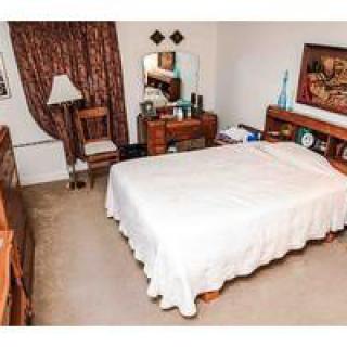 A cozy bedroom with wooden furniture, including a bed, dresser, chair, and lamp.