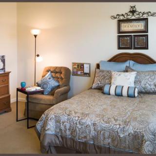 A cozy bedroom with a neatly made bed, an upholstered chair, and a standing lamp.