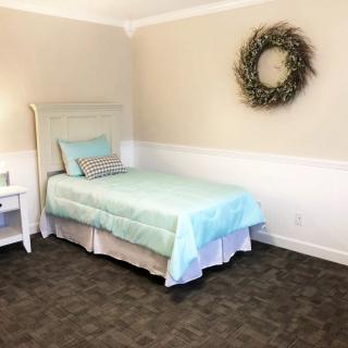 A minimalist bedroom with a pastel-colored single bed and a wreath hanging on the wall.