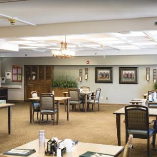 A well-lit dining area with tables and chairs arranged on a carpeted floor.