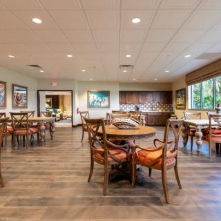 An indoor dining area with wooden flooring, tables and chairs, ceiling lights, and large windows.