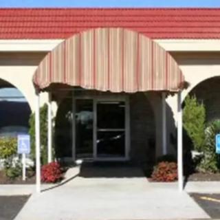 A building entrance with a striped awning and glass door surrounded by plants.