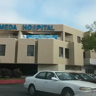A hospital building with a visible parking lot and a car in the foreground.