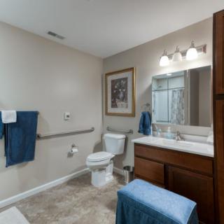 A well-lit bathroom with accessible features, including a grab bar by the toilet and blue towels accenting the decor.