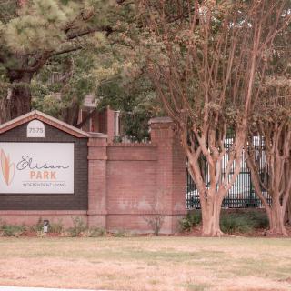Entrance sign for Sheridan Park Apartments surrounded by trees and landscaping.